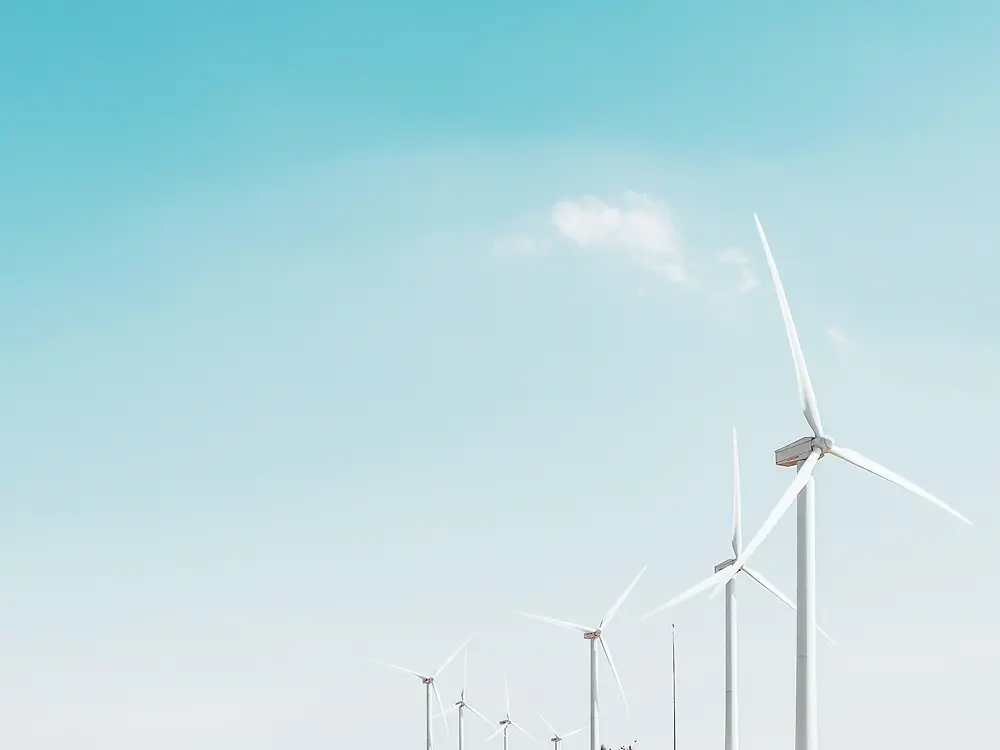 a row of wind turbines against a pale blue sky