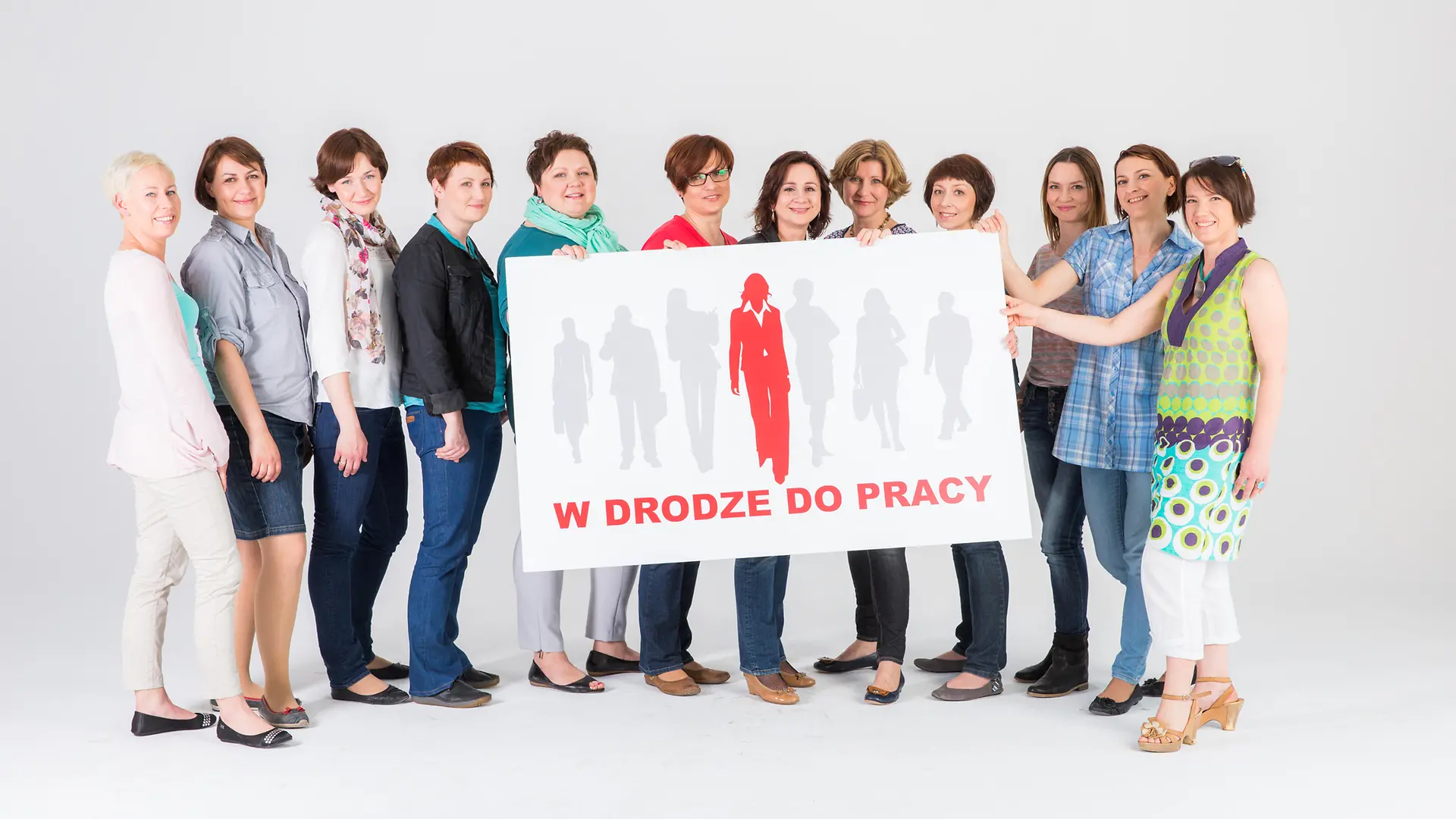 Mehrere Frauen stehen zusammen und halten ein Schild mit der Aufschirft „W drodze do pracy”