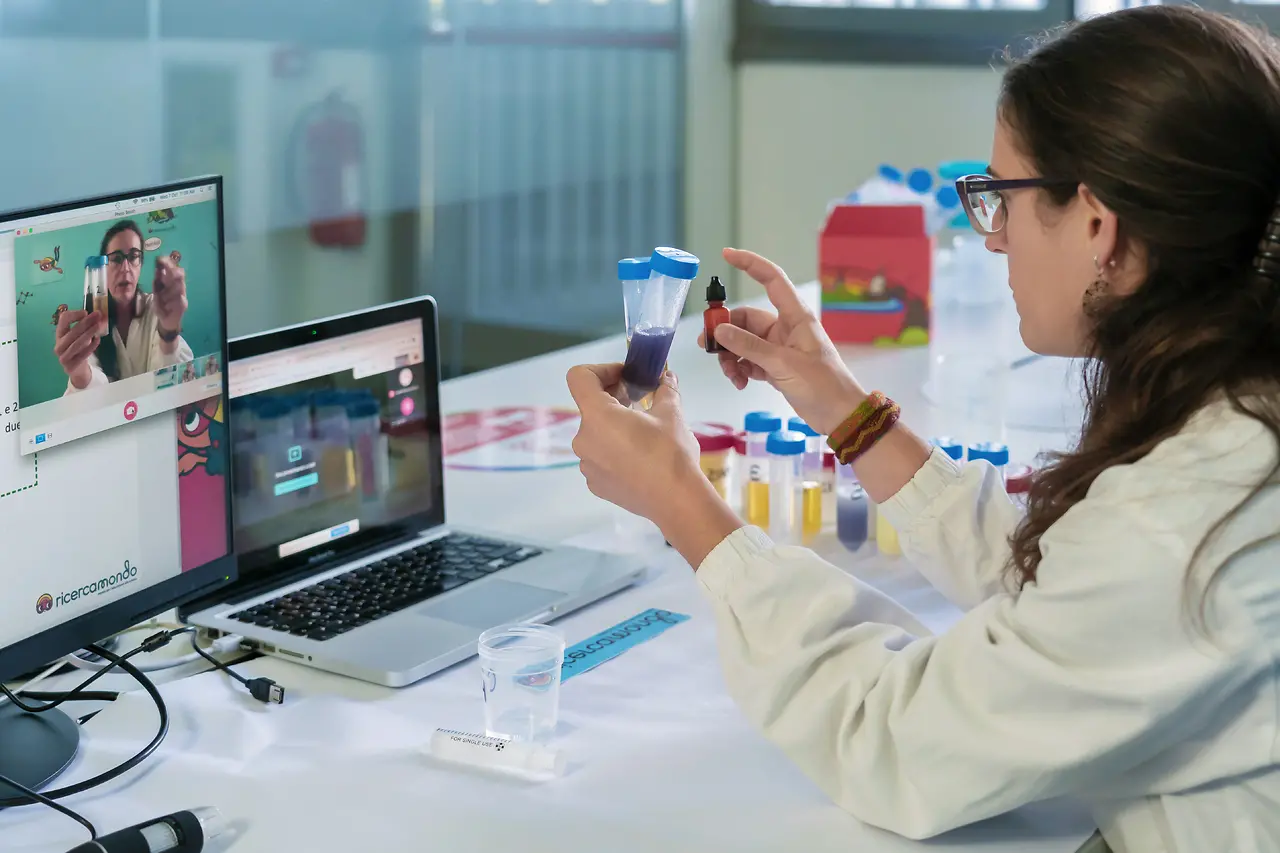 woman sitting infront of laptop holding tubes in front of computer webcam