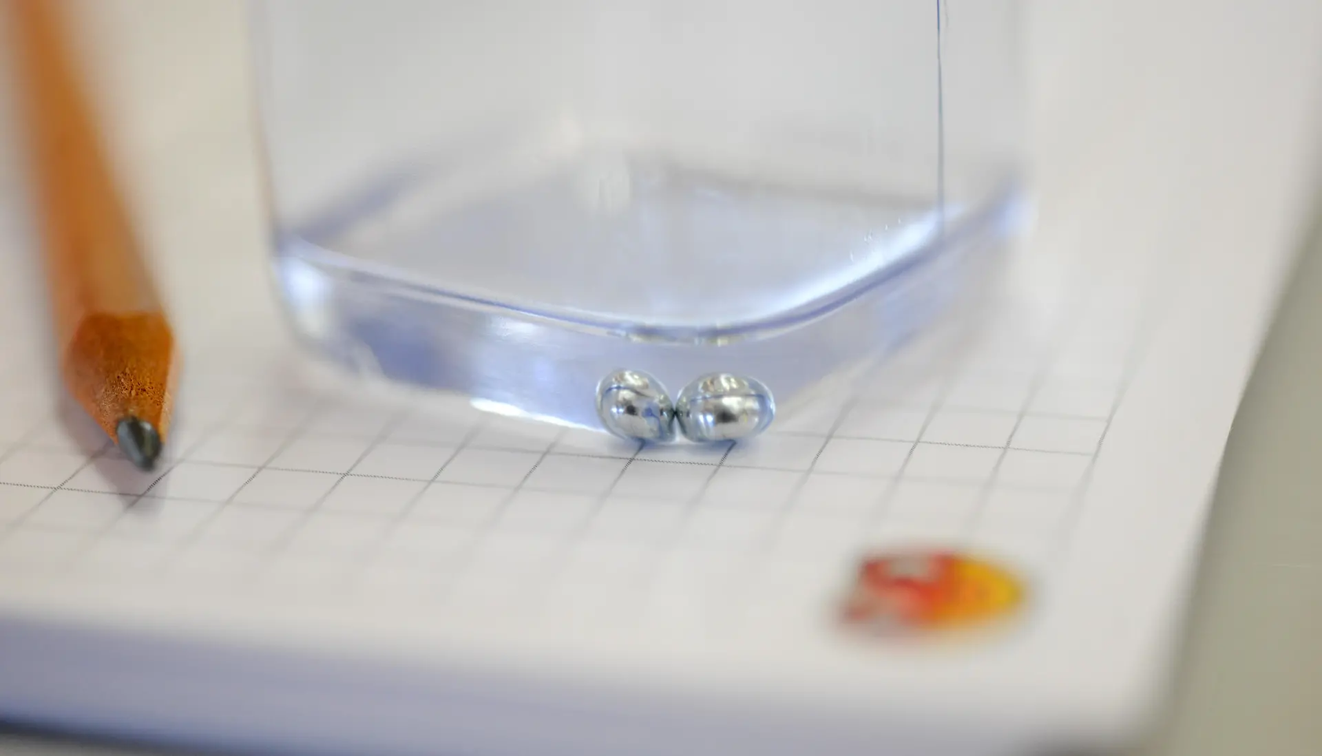 lower half of small container with a clear liquid standing on checkered paper