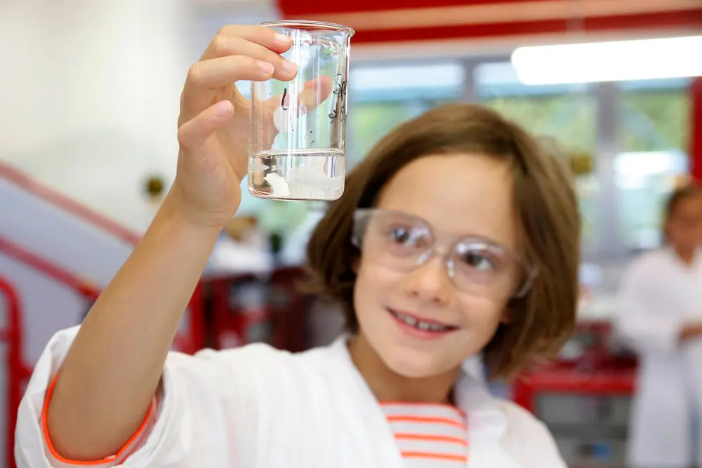 girl in lab coat looks at liquid in beaker