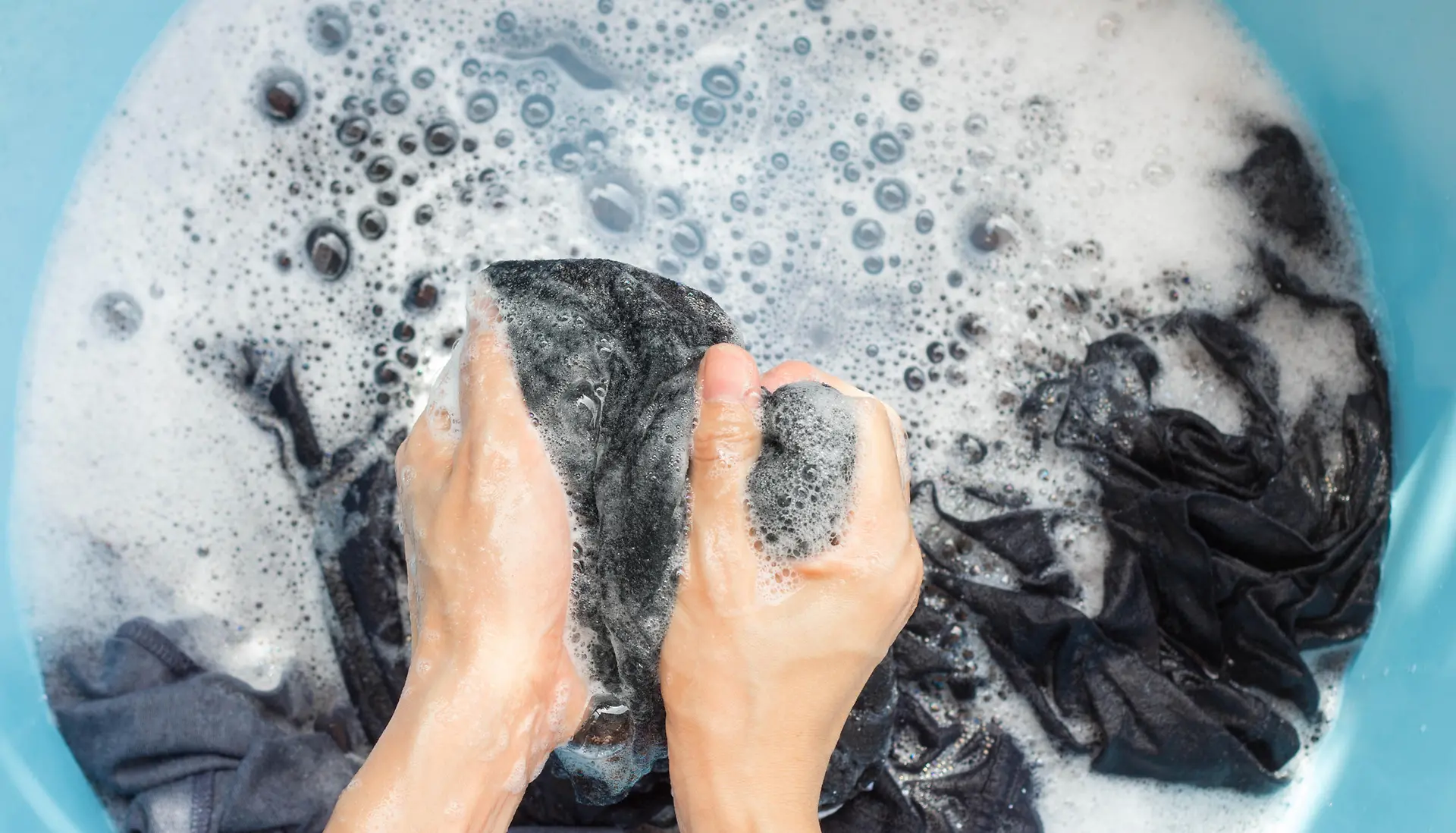 hands washing fabric in plastic bowl