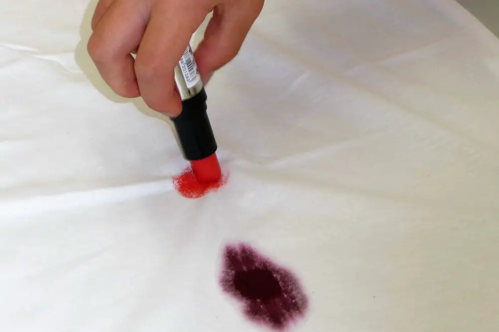 hand applying red lipstick on white fabric