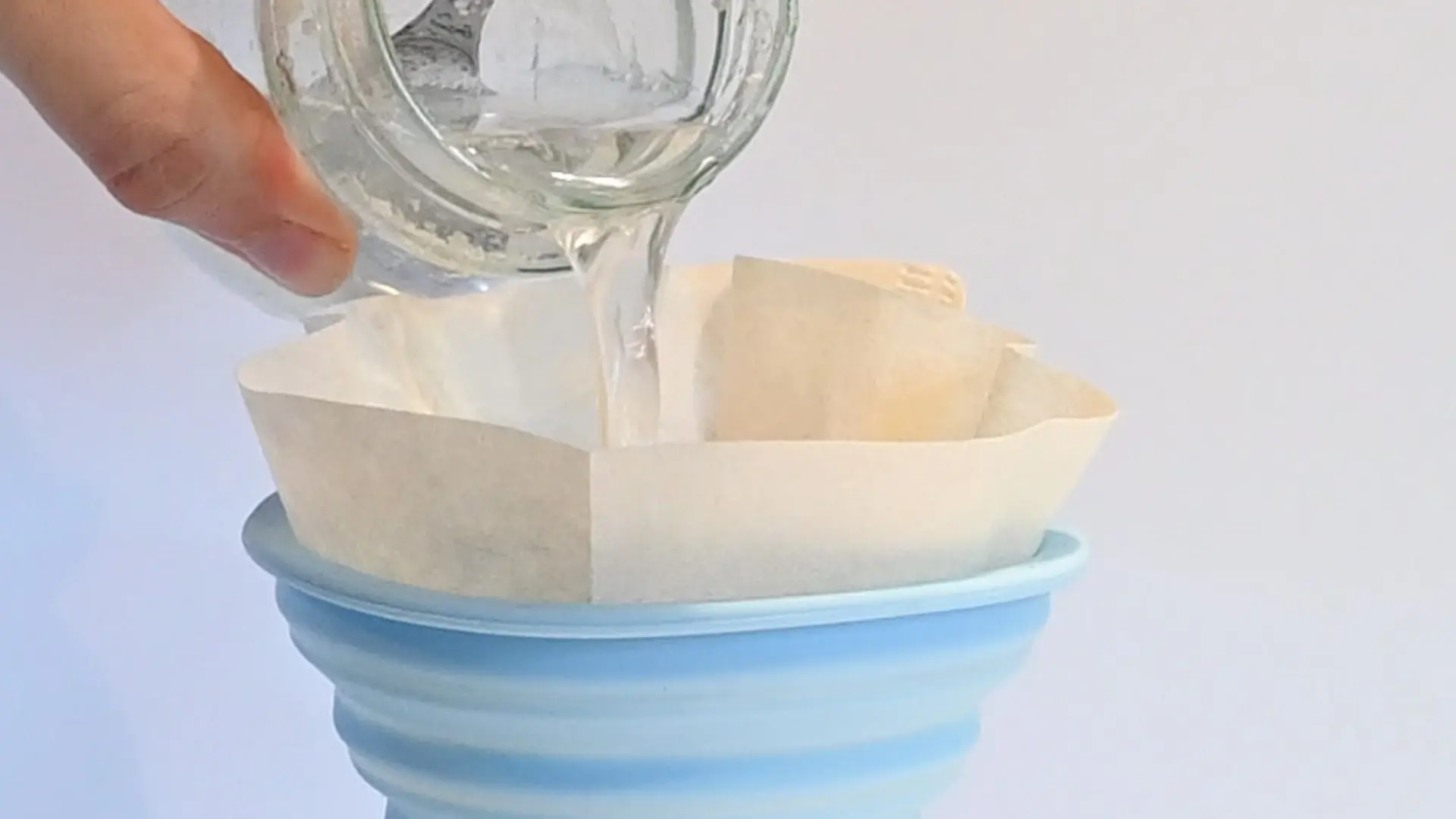 hand pours liquid through filter in glass jar