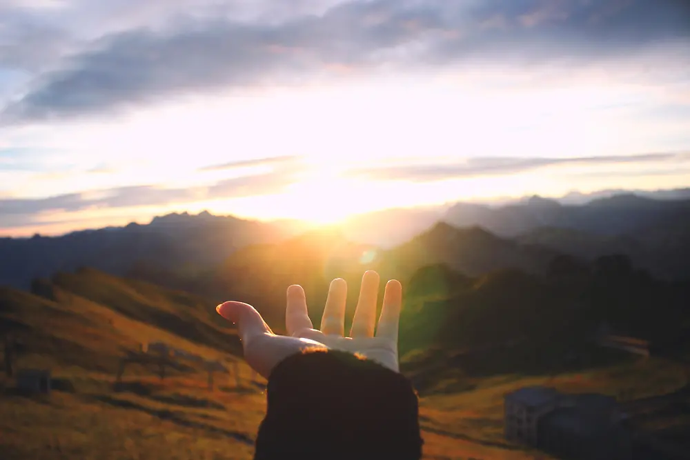 Hand reaching out towards the sunrise