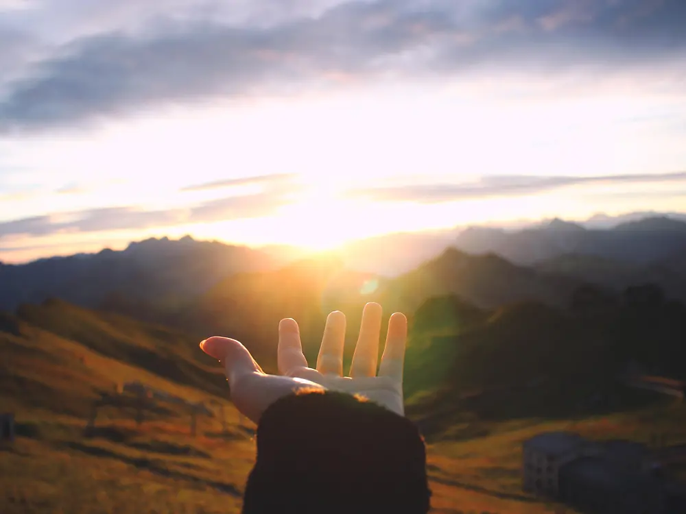 Hand reaching out towards the sunrise