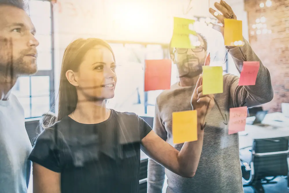 Three employees brainstorm together, collect their ideas on sticky notes and exchange them.