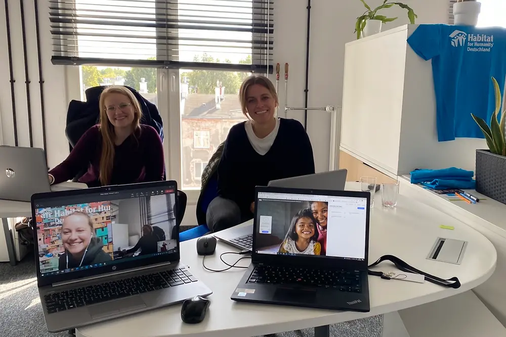 Zwei Frauen sitzen am Schreibtisch, zwei weitere Frauen sind am Laptop zugeschaltet.