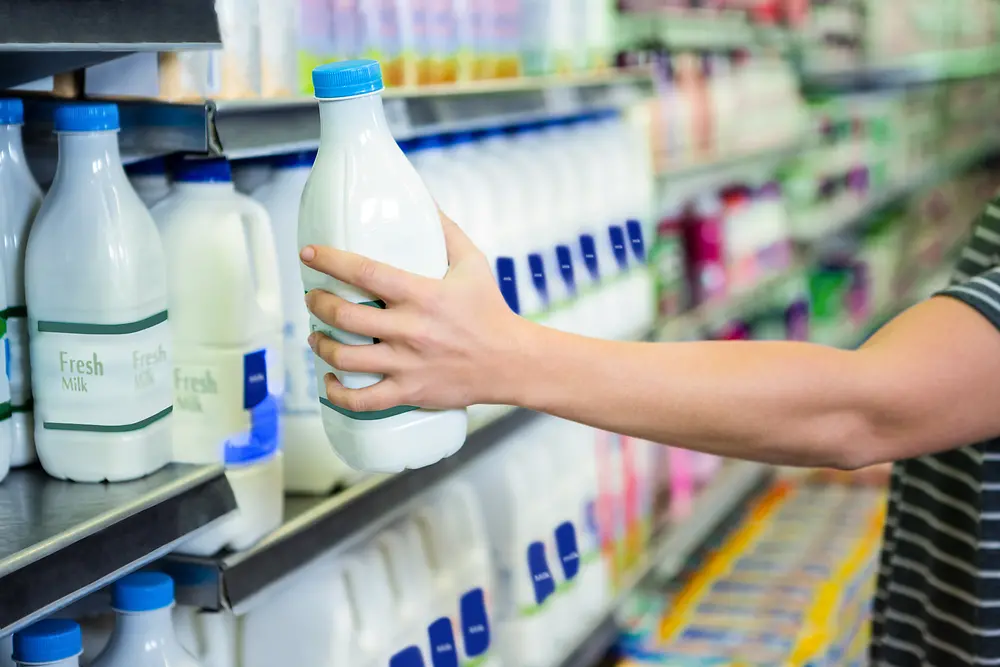 Hand grabs milk bottle in supermarket shelf.