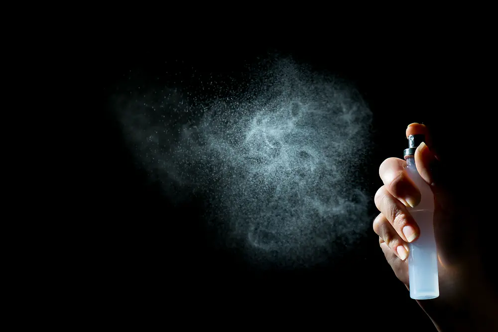 Hand with pump spray, white mist on black background