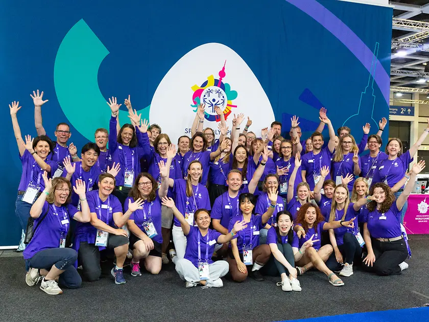 Das internationale Team von 60 Henkel-Freiwilligen steht jubelnd vor dem Banner der Special Olympics World Games in Berlin.