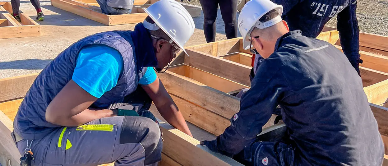 Zwei Henkel-Mitarbeiter begutachten die Bauteile für das Holzgerüst des Hauses.